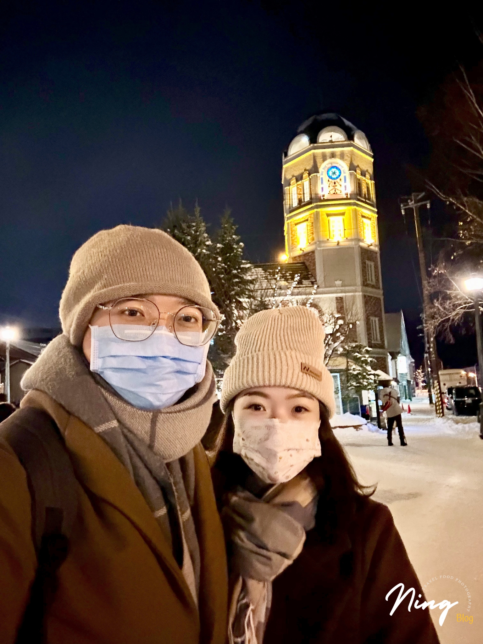 小樽音樂盒堂前夜景，一對旅人在鐘樓前合照